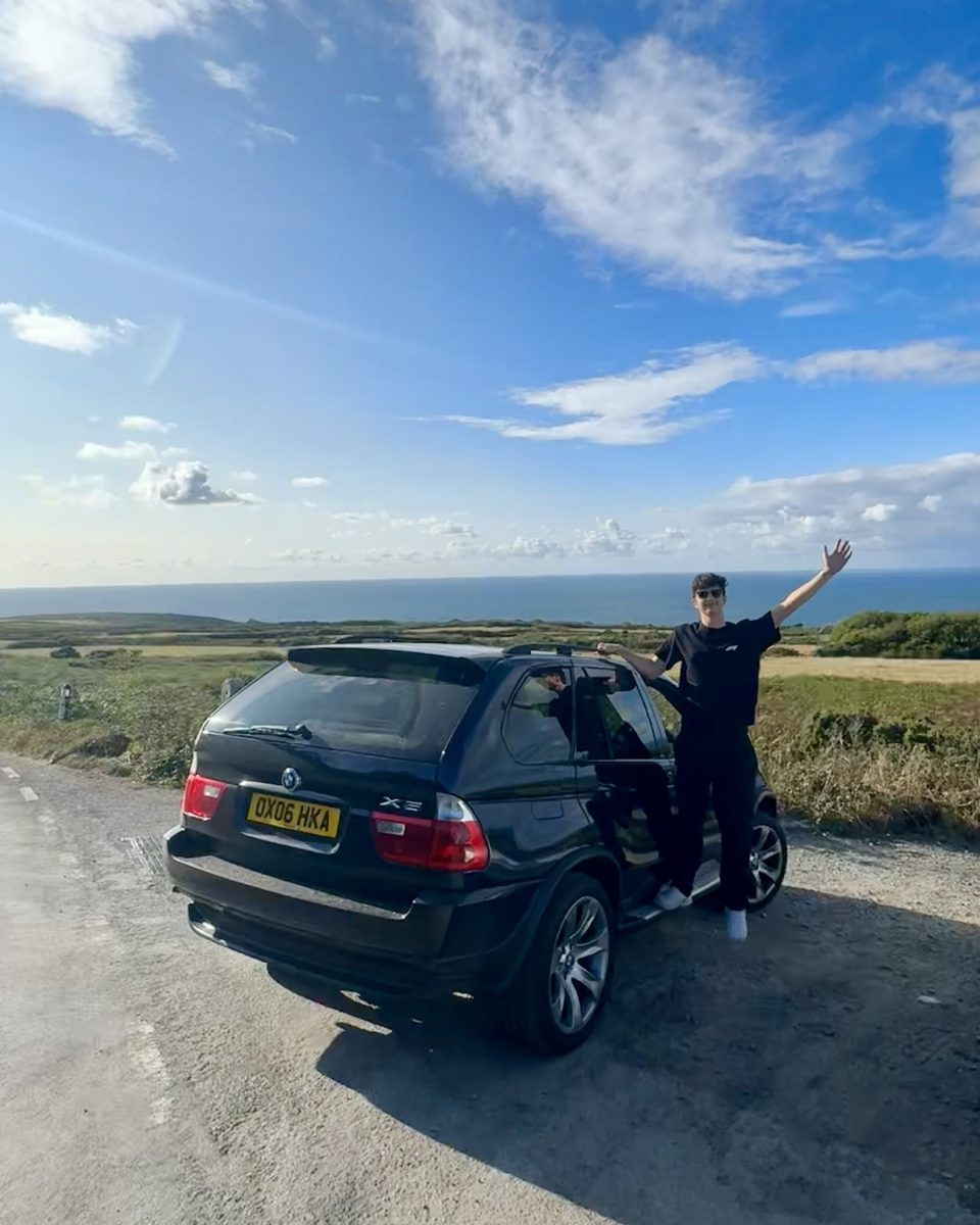 Elanas, founder of Lucido Detailing, beside a black BMW X5 on a coastal road